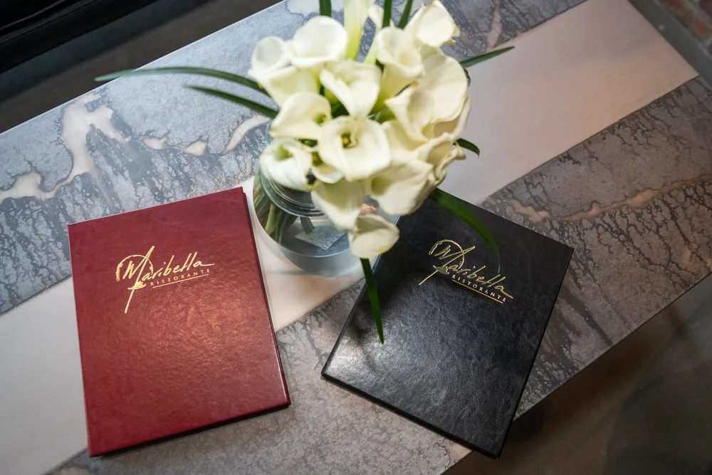 Maribella menu covers in oxblood and black leather on a marble table