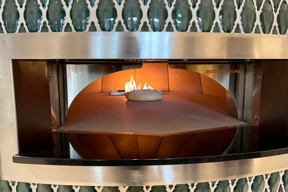 The wood-fired oven at Maribella, set into a wall of sage green tile